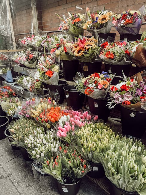 An outdoor display of numerous floral bouquets arranged in black buckets. The bouquets feature a variety of flowers including pink tulips, white tulips, orange tulips, and mixed blooms with red, purpl